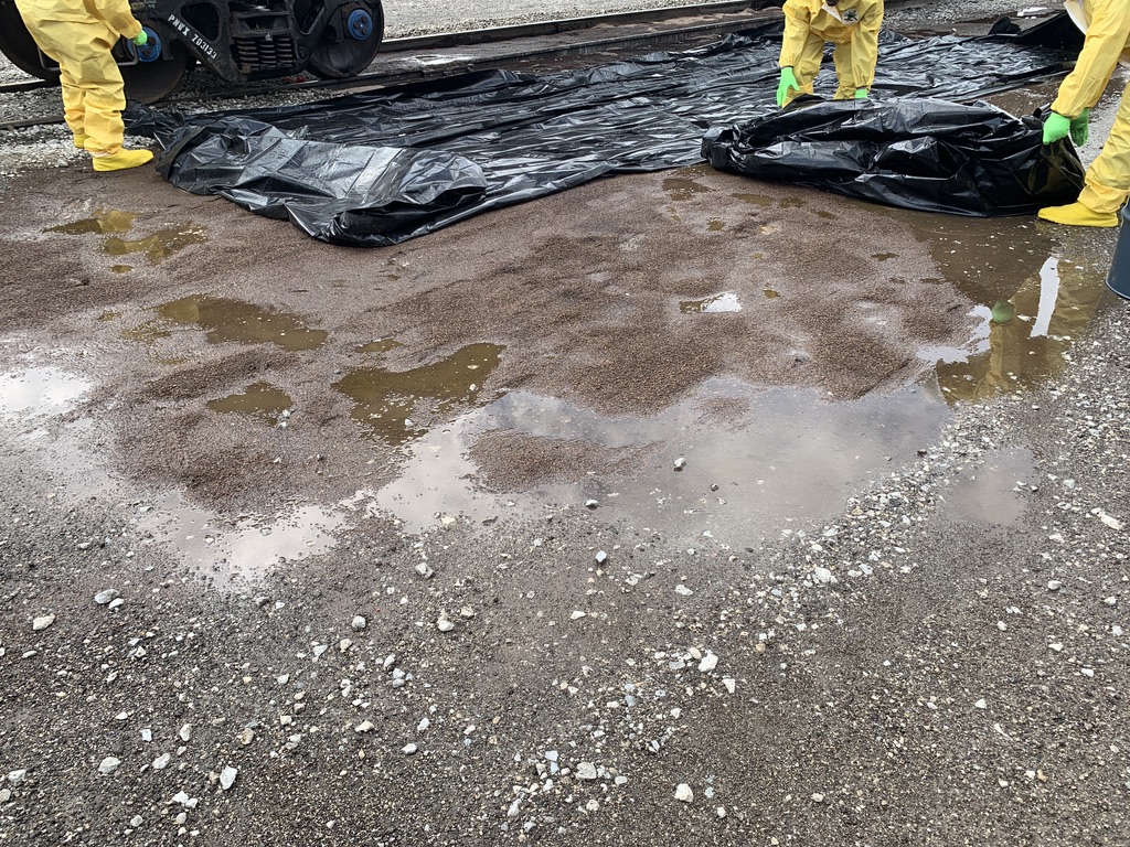 Cleanup Crew lays tarp down to begin remediation of a spill